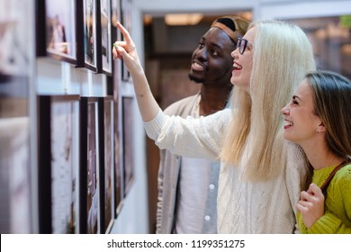 Three young people hipster students with different skins looking happy together, talkng, looking at picture on wall, spending free time together in art photo gallery. Multi ethnic, friendship concept.