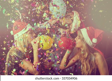 Three Young People At New Year's Eve Party On Midnight Blowing Colorful Balloons And Having Fun