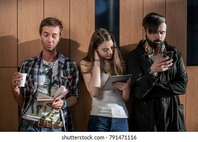 Three Young People Standing Near The Wall With Gadgets In Their Hands. Two Boys And One Girl.