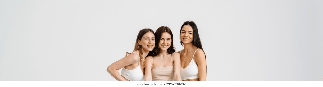 Three young positive smiling attractive ladies pose and hold poster standing in studio isolated over white background