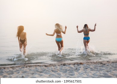 Three young pretty woman in a bathing suit running along the sandy beach into the sea. Back view. Rest on the sea, sunbathing, healthy lifestyle. - Powered by Shutterstock