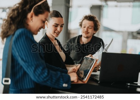 Three young professionals collaborating on a project using a tablet and laptop in a modern office setting.