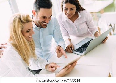 Drei junge lächelnde Kollegen arbeiten zusammen auf Laptop