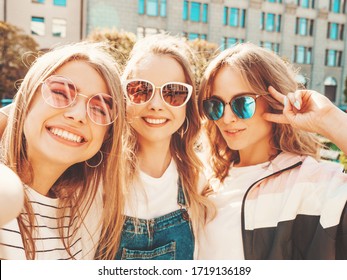 Three young smiling hipster women in summer clothes.Girls taking selfie self portrait photos on smartphone.Models posing in the street.Female showing positive face emotions 