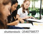 Three young students focused on writing at a table. Diverse group of girls engaged in study. Concentrated students working on assignments together. Education and knowledge. 