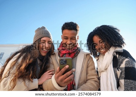 Three young students are having fun watching something on a smartphone in winter