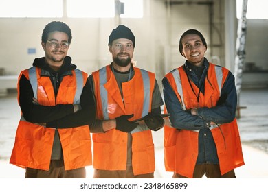 Three young successful engineers of industrial factory or workers of warehouse in safety vests crossing their arms by chest and looking at you - Powered by Shutterstock