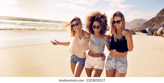 Three young and vibrant female friends walk on the seashore, laughing and enjoying each other's company. Happy young women having fun at the beach in summer, celebrating friendship and good times. - Powered by Shutterstock