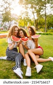 Three Young Woman  Camping On The Grass, Eating Watermelon, Laughing. People, Lifestyle, Travel, Nature And Vacations Concept. Summer Concept.