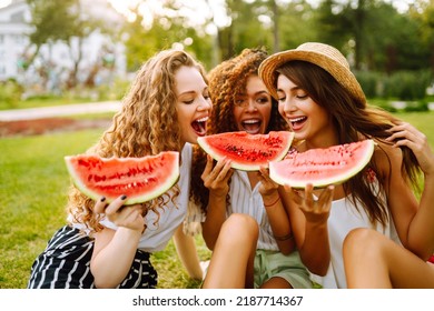 Three Young Woman  Camping On The Grass, Eating Watermelon, Laughing. People, Lifestyle, Travel, Nature And Vacations Concept.