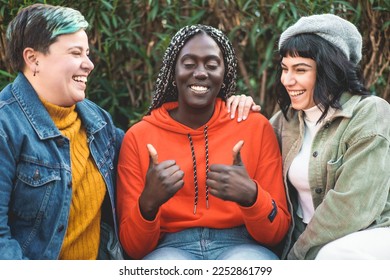 Three young women, an African woman with dreadlocks, a curvy woman with non-binary gender, spending time together chatting and having fun. The African woman is in the center, thumbs up - Shutterstock ID 2252861799