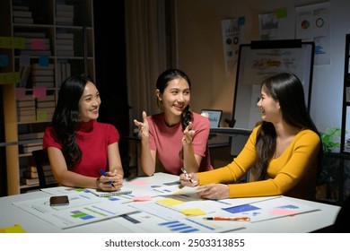 Three young women discussing ideas and working together in a modern office setting during a nighttime meeting. - Powered by Shutterstock