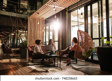 Three Young Women Discussing New Business Ideas While Sitting On Creative Office. Modern Office Lobby With Business People Doing Meeting.