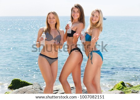 Three young women friends in bikini holding water bottles on the sandy beach. Focus on all persons 