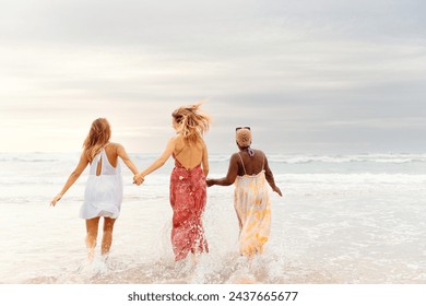 three young women holding hands walking towards the sea on a summer's day - Powered by Shutterstock