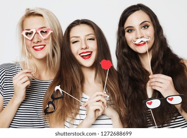 Three young women holding paper party sticks 