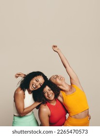 Three young women laughing happily as they stand together in a studio wearing sports clothing. Group of female friends celebrating their fit, healthy and sporty lifestyle. - Shutterstock ID 2265470573