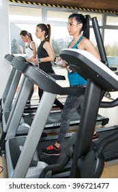 Three Young Women Running On Treadmill In Gym.