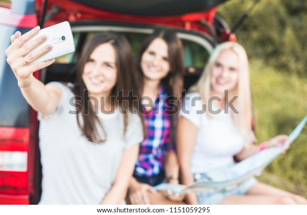 Three\
young women with suitcases on a trip by car. They sit in the back\
of the car, they look at the map, resting after a long drive and\
having fun. Hitchhiking and car trips with\
friends