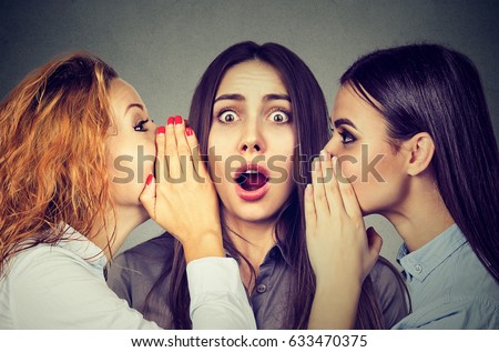 Three young women telling whispering a secret gossip each other in the ear 