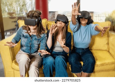 Three young women, two Caucasian and one Brazilian, aged 20-30, sitting on a couch in a gaming lounge, wearing VR headsets and using hand tracking technology. Casually dressed.