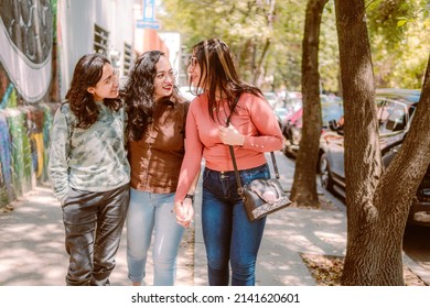 Three Young Women Are Walking Down The Street, They Are Smiling, Playing And Having A Good Time.