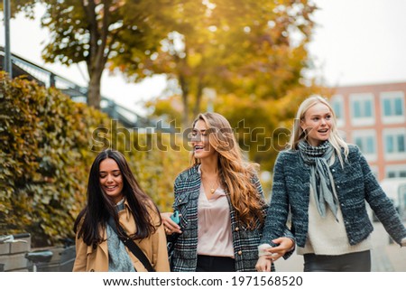 Three young women walking together trough city. 