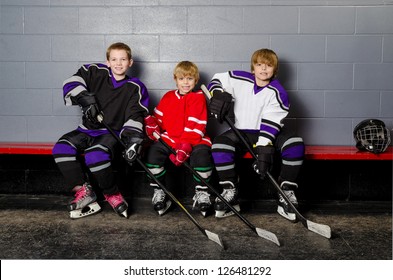 Three Youth Boys Hockey Players Pose in Dressing Room in their equipment