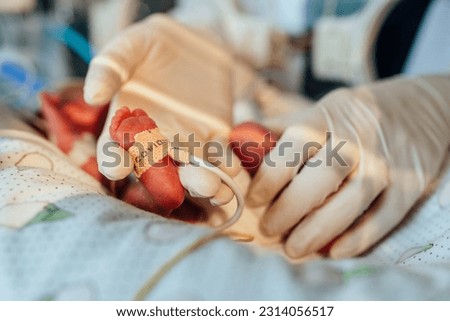 Three-day-old newborn baby in intensive care unit in a medical incubator. Macro photo of doctor's hand in gloves holding legs of child. Newborn rescue concept.