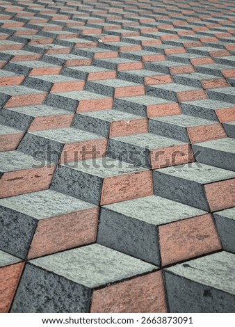 A three-dimensional geometric patterned floor with a combination of gray, black, and brick red creates the optical illusion of a cube.