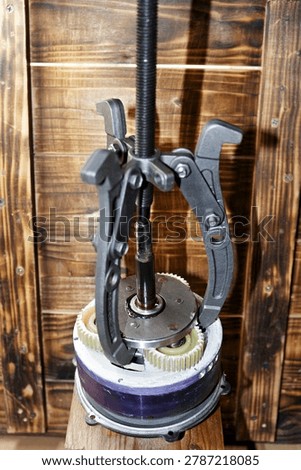 Three-jaw gear puller removing an overrunning clutch from an electric bicycle motor hub for maintenance and mechanical repair on a rustic wooden workshop background