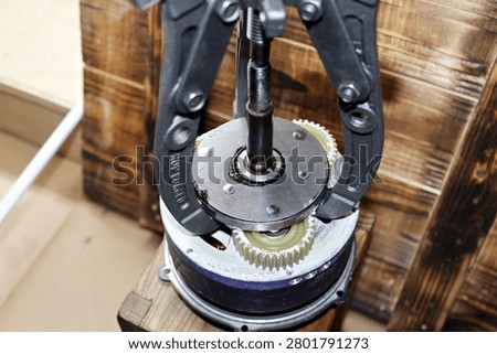 Three-jaw gear puller removing an overrunning clutch from a geared electric bike motor, professional workshop maintenance and repair process of e-bike hub motor internals on a wooden table