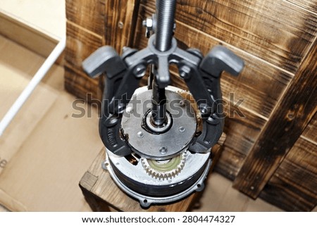 Three-jaw gear puller removing an overrunning clutch from an electric bicycle motor wheel hub, showing technical maintenance and mechanical repair process in a home workshop setting