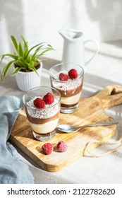 Three-layer mousse dessert made of chocolate and vanilla, decorated with fresh raspberries and coconut flakes in glasses on the table. Brunch, dessert for lovers - Shutterstock ID 2122782620