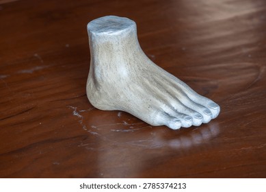 Three-quarter angle view of a white plaster human foot sculpture model for fine art and anatomy study on a wooden table background