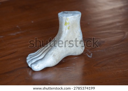 Three-quarter angle view of a white plaster human foot sculpture model for fine art and anatomy study on a wooden table background