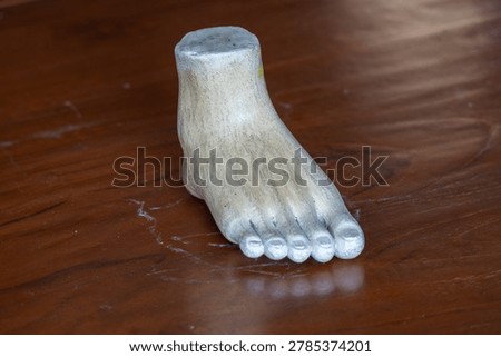 Three-quarter angle view of a white plaster human foot sculpture model for fine art and anatomy study on a wooden table background