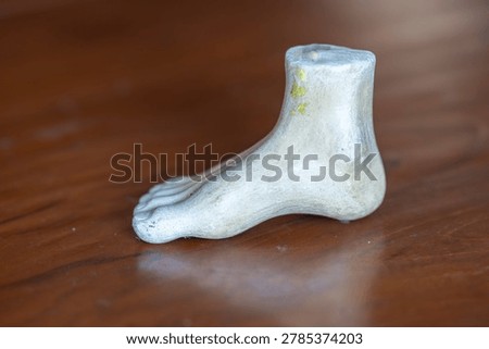 Three-quarter angle view of a white plaster human foot sculpture model for fine art and anatomy study on a wooden table background