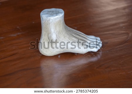 Three-quarter angle view of a white plaster human foot sculpture model for fine art and anatomy study on a wooden table background