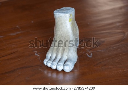 Three-quarter angle view of a white plaster human foot sculpture model for fine art and anatomy study on a wooden table background