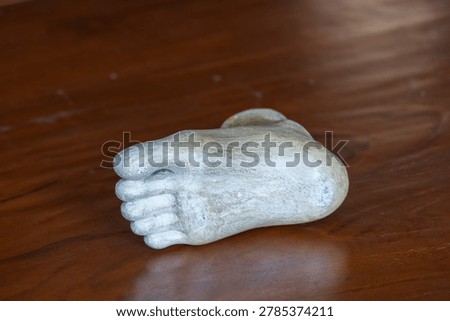 Three-quarter angle view of a white plaster human foot sculpture model for fine art and anatomy study on a wooden table background