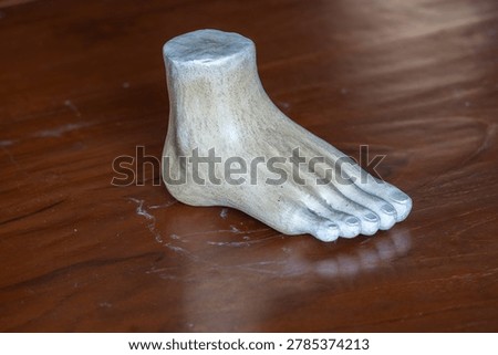 Three-quarter angle view of a white plaster human foot sculpture model for fine art and anatomy study on a wooden table background