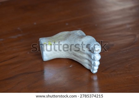 Three-quarter angle view of a white plaster human foot sculpture model for fine art and anatomy study on a wooden table background