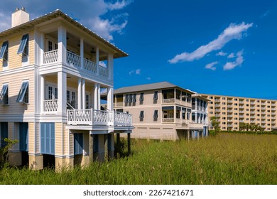 Three-storey homes and apartments on the beach near the grasses at Destin Point, Destin, Florida. There are houses over the tall grasses with balconies along the multi-storey apartment on the right.