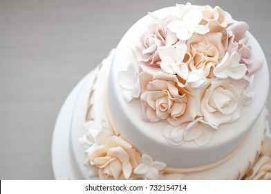 Three-tiered White Wedding Cake Decorated With Flowers From Mastic On A White Wooden Table. Picture For A Menu Or A Confectionery Catalog. Top View.