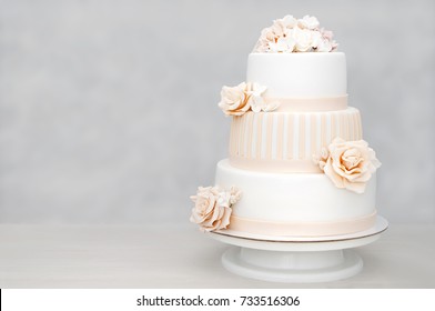 Трехуровневый белый свадебный торт украшен цветами из мастики на белом деревянном столе. Картинка для меню или каталога кондитерских изделий с копировальным пространством.