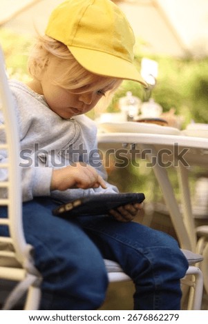 Three-year-old boy in a yellow cap playing a game on a smartphone, children and gadgets