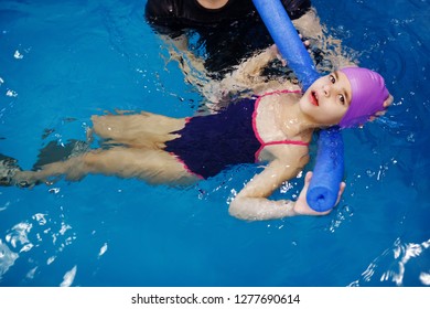 Three-year-old child in a blue cap and swimming glasses is bathed in a pool with the help of a male instructor. Aquatherapy. Water Rehabilitation. Diving. Healthy lifestyle. - Powered by Shutterstock