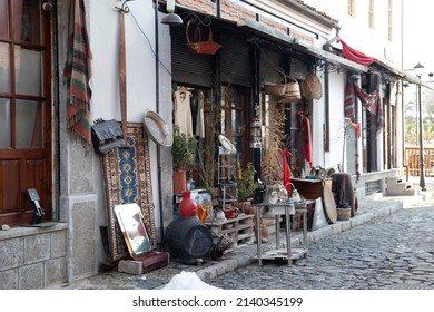 Thrift Store On A Side Street In The Historic Neighborhood Of Korce, Albania. The Old Ottoman Bazaar. Items For Sale On The Sidewalk.