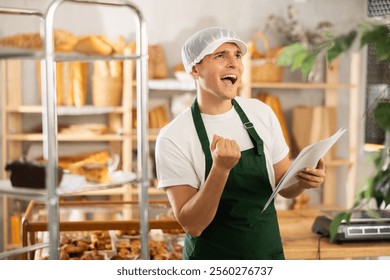 Thrilled entrepreneur in green apron reacting with excitement while reviewing financial documents showing increased profits in small artisan bakery - Powered by Shutterstock